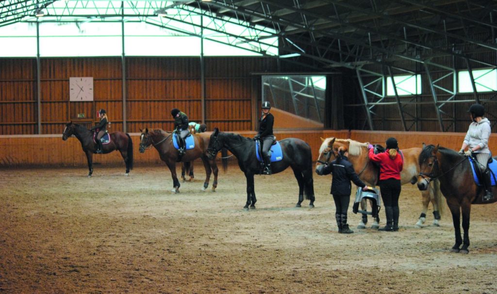 Henkilöitä hevosten selässä ratsastustunnilla.